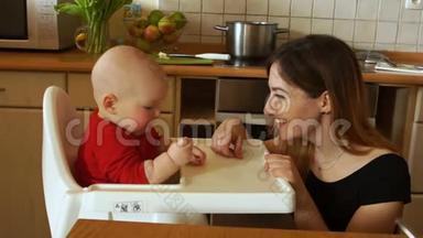 母亲在厨房的高脚椅上喂饥饿的婴儿。那女人对婴儿温和地微笑。母亲节